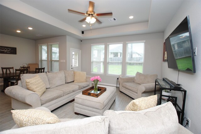 living room with a tray ceiling, ceiling fan, and light hardwood / wood-style floors