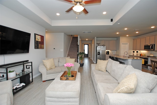 living room with light wood-type flooring, ceiling fan, and a raised ceiling