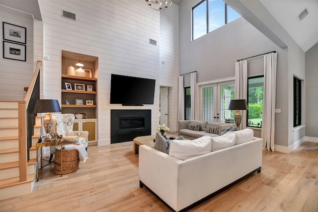 living room with built in features, light wood-type flooring, and high vaulted ceiling