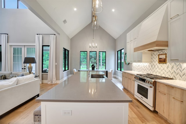 kitchen featuring high end stove, premium range hood, a kitchen island with sink, and light brown cabinets