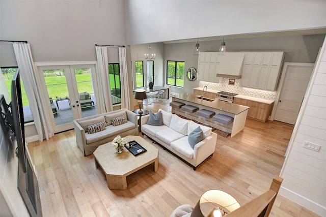 living room featuring a notable chandelier, light hardwood / wood-style flooring, a wealth of natural light, and french doors