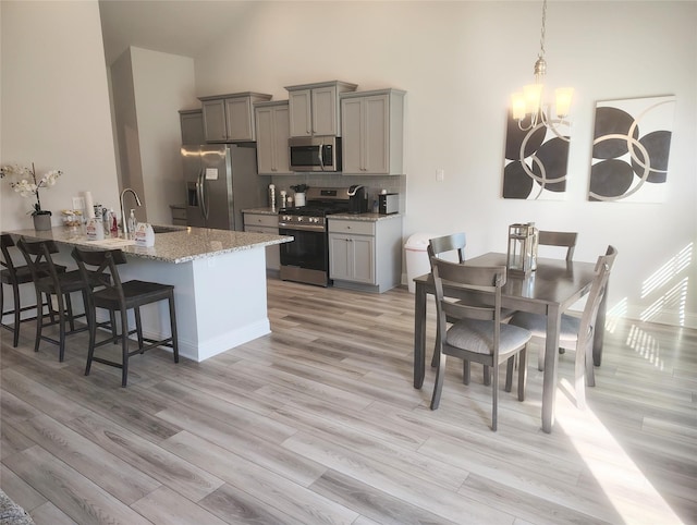 kitchen with appliances with stainless steel finishes, a kitchen breakfast bar, gray cabinetry, and light stone countertops