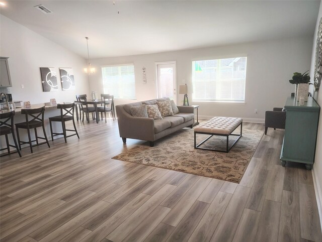 living room with a chandelier, lofted ceiling, visible vents, and wood finished floors
