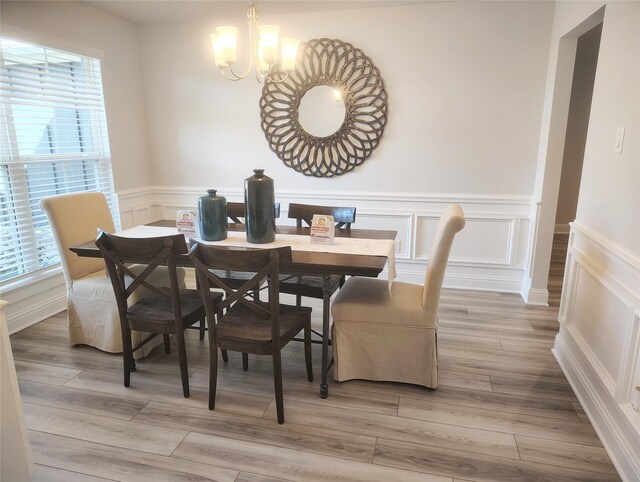 dining area featuring light wood finished floors, a decorative wall, an inviting chandelier, and wainscoting
