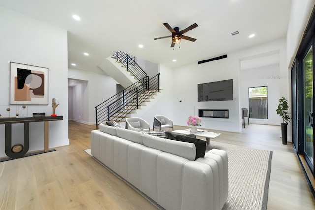 living area featuring stairway, visible vents, light wood finished floors, recessed lighting, and a glass covered fireplace