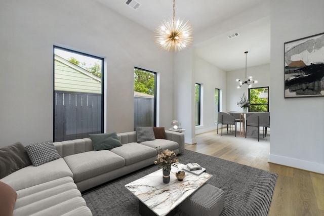 living area with a wealth of natural light, visible vents, an inviting chandelier, and wood finished floors