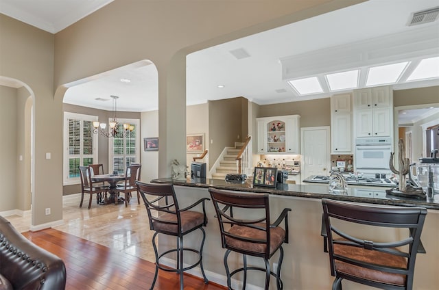 22222 Holly Creek Trl, Tomball, TX 77377 - kitchen featuring a breakfast bar area, decorative backsplash, glass insert cabinets, crown molding, and a chandelier