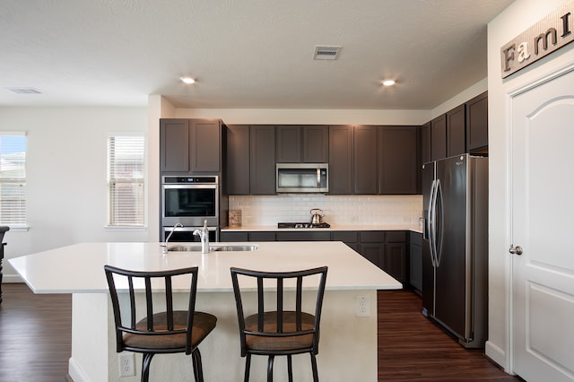 kitchen featuring decorative backsplash, stainless steel appliances, dark hardwood / wood-style floors, and a center island with sink