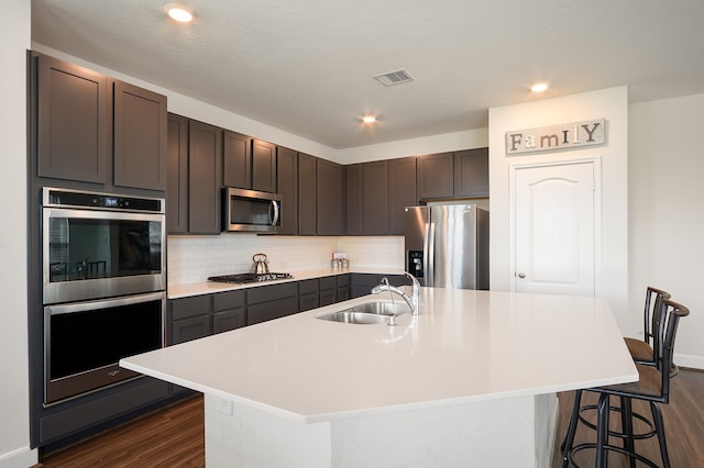 kitchen with appliances with stainless steel finishes, dark hardwood / wood-style floors, and a kitchen island with sink