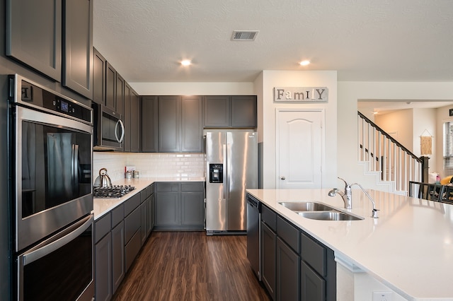 kitchen featuring appliances with stainless steel finishes, sink, gray cabinetry, backsplash, and dark wood-type flooring