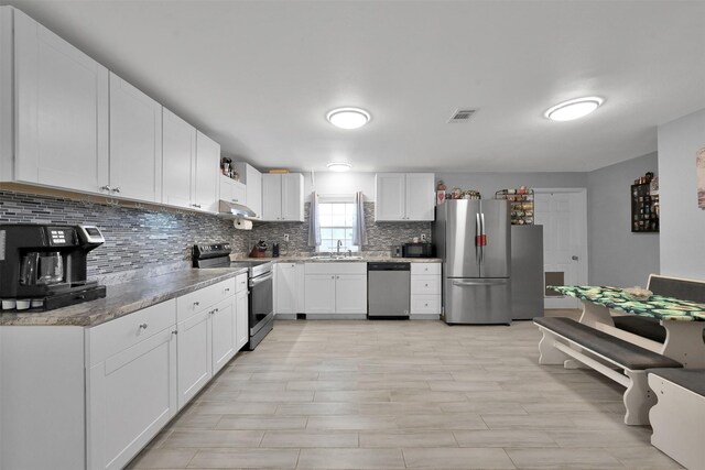 kitchen with white cabinets, light stone counters, appliances with stainless steel finishes, decorative backsplash, and sink