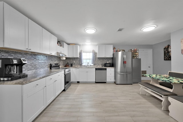 kitchen with sink, white cabinets, decorative backsplash, light stone counters, and stainless steel appliances