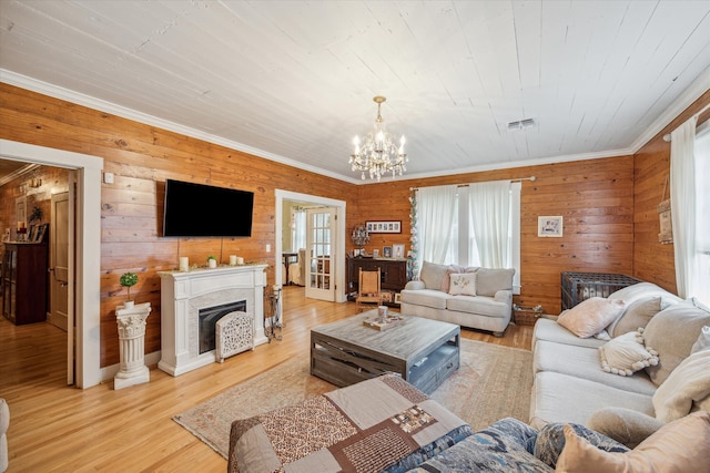 living room with wood walls, ornamental molding, an inviting chandelier, and light wood-type flooring