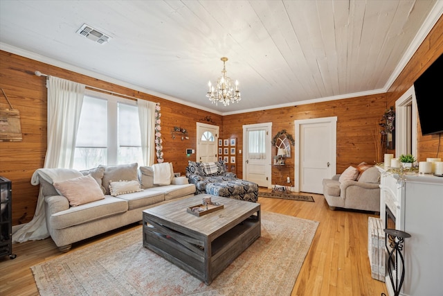 living room featuring light hardwood / wood-style floors, a notable chandelier, ornamental molding, and wooden walls