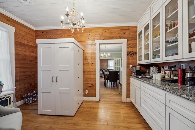 kitchen with dark stone countertops, wooden walls, an inviting chandelier, white cabinets, and light hardwood / wood-style floors