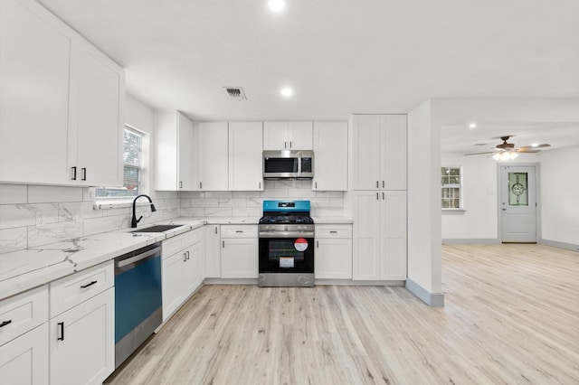 kitchen featuring appliances with stainless steel finishes, sink, white cabinets, decorative backsplash, and light stone countertops