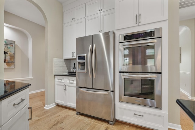 kitchen featuring appliances with stainless steel finishes, white cabinetry, dark stone countertops, backsplash, and light hardwood / wood-style floors