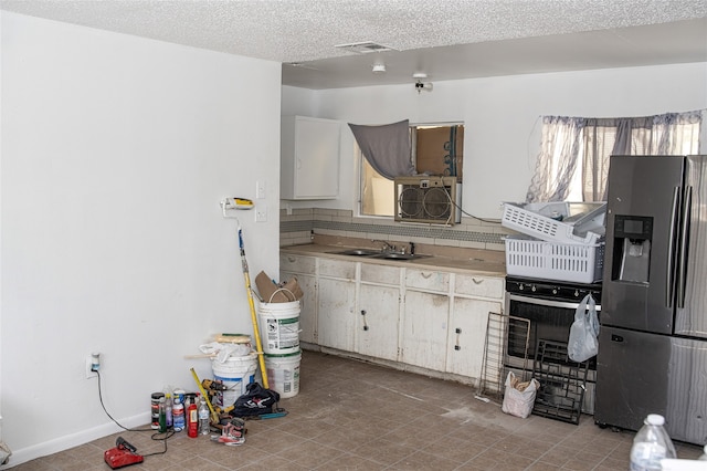 kitchen with sink, light tile patterned flooring, stainless steel refrigerator with ice dispenser, and a textured ceiling