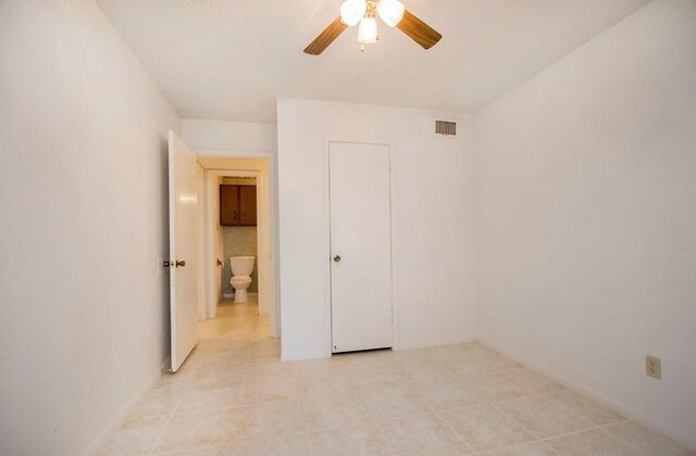 unfurnished bedroom with connected bathroom, light tile patterned floors, and ceiling fan