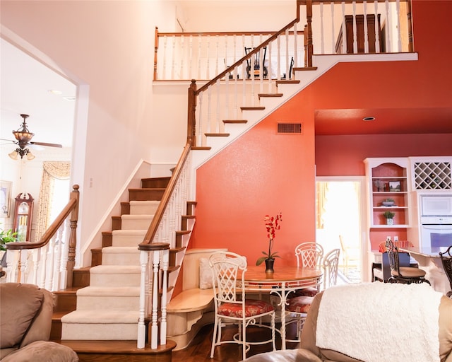 stairs with wood-type flooring, a high ceiling, and ceiling fan