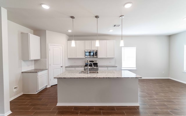 kitchen with a center island with sink, appliances with stainless steel finishes, light stone counters, and white cabinetry