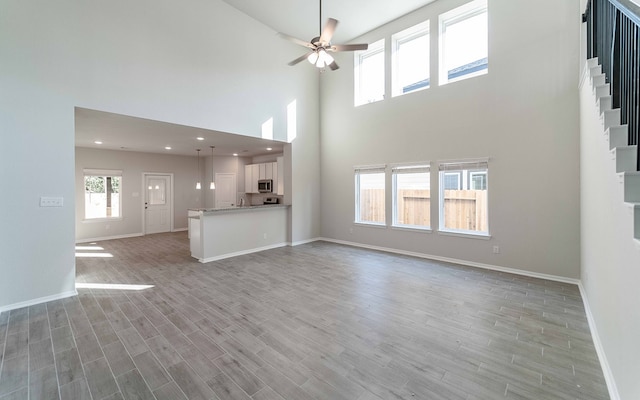 unfurnished living room featuring ceiling fan, light wood-type flooring, and a high ceiling