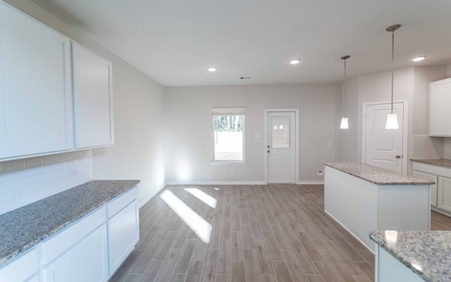 kitchen with pendant lighting, white cabinets, light stone counters, and light wood-type flooring