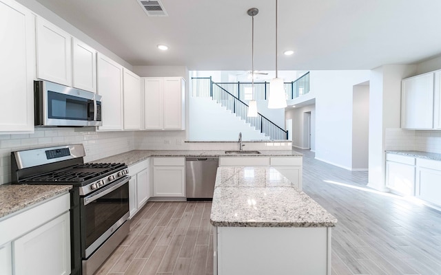 kitchen with light hardwood / wood-style floors, decorative light fixtures, stainless steel appliances, and white cabinets