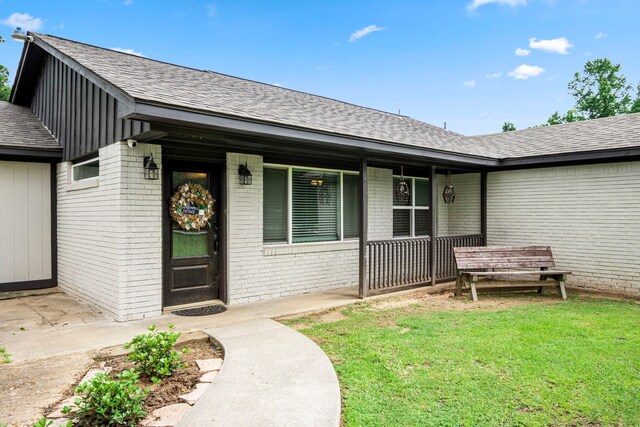 view of exterior entry with a lawn and a porch