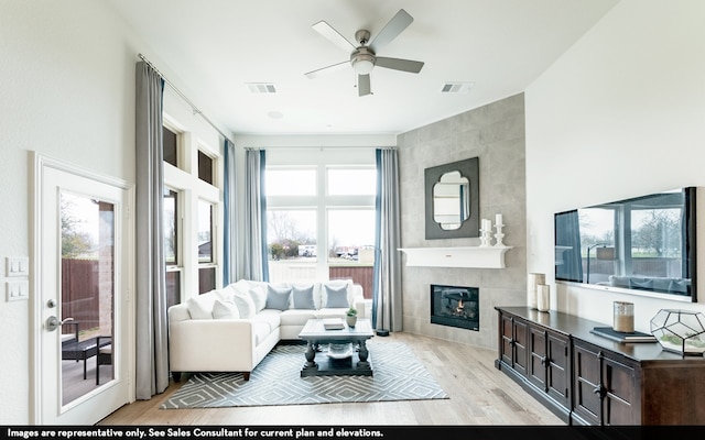 living room with light hardwood / wood-style flooring, a tiled fireplace, ceiling fan, and tile walls