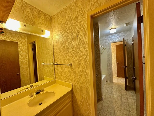 bathroom featuring a textured ceiling, vanity,  shower combination, and tile patterned flooring