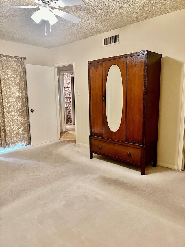 unfurnished bedroom with baseboards, visible vents, a ceiling fan, light colored carpet, and a textured ceiling