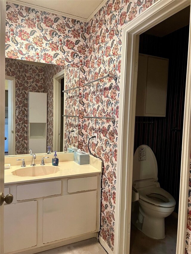 bathroom with vanity, toilet, and wallpapered walls