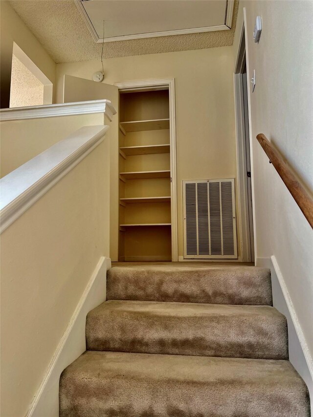 staircase with a textured ceiling, visible vents, and attic access