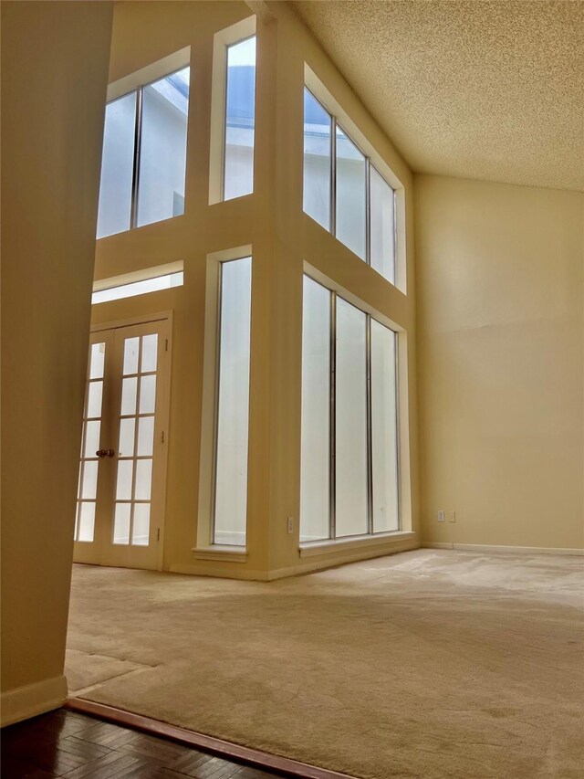 unfurnished living room featuring a high ceiling, a textured ceiling, french doors, and carpet flooring