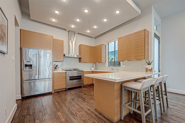 kitchen featuring dark hardwood / wood-style flooring, kitchen peninsula, a kitchen breakfast bar, wall chimney exhaust hood, and high end appliances