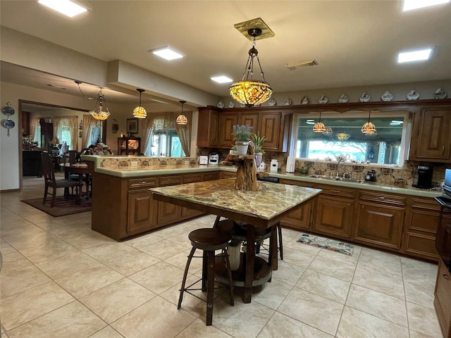 kitchen with tasteful backsplash, sink, kitchen peninsula, pendant lighting, and light tile patterned floors