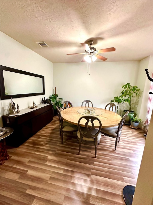 dining room with ceiling fan, wood-type flooring, and a textured ceiling