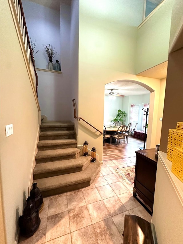 stairway featuring a high ceiling, tile patterned floors, and ceiling fan