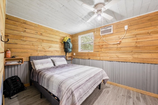 bedroom with a wall mounted AC, wood-type flooring, wooden walls, and ceiling fan