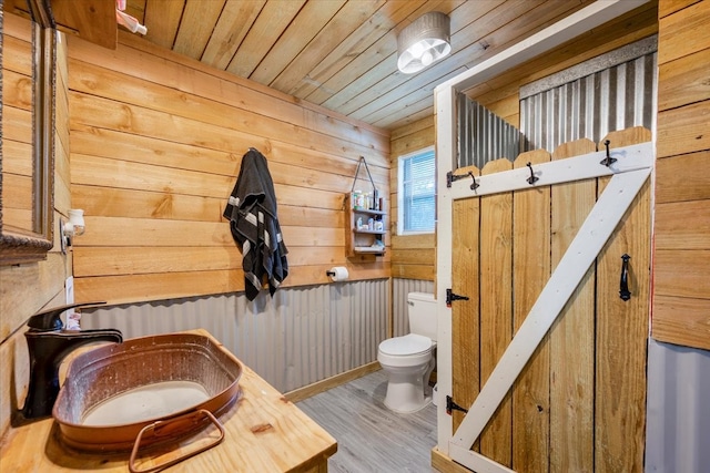 bathroom with wood-type flooring, sink, wood walls, toilet, and wood ceiling