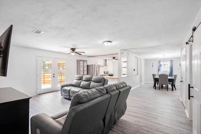 living room featuring a barn door, french doors, light wood-type flooring, and ceiling fan