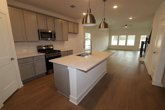 kitchen with pendant lighting, sink, stainless steel appliances, dark hardwood / wood-style floors, and a center island with sink