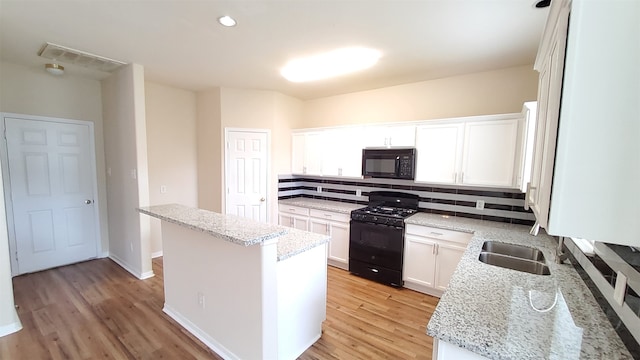 kitchen featuring light hardwood / wood-style flooring, white cabinets, black appliances, a center island, and backsplash