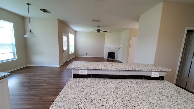 kitchen featuring dark wood-type flooring, light stone countertops, a kitchen island, ceiling fan, and decorative light fixtures