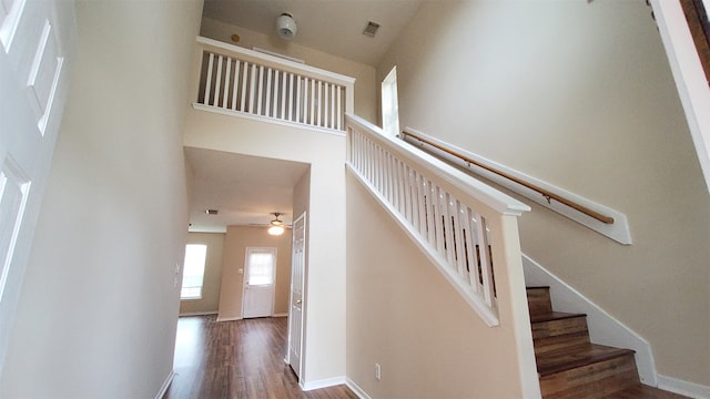 stairs with hardwood / wood-style floors, a towering ceiling, and ceiling fan