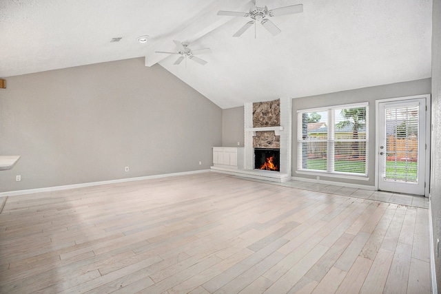 unfurnished living room featuring vaulted ceiling with beams, a stone fireplace, light wood-type flooring, and a textured ceiling