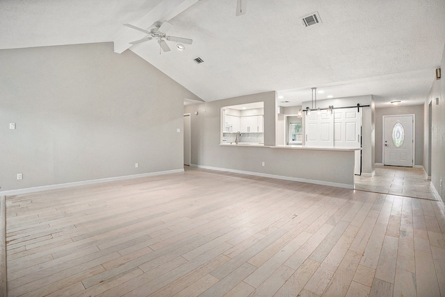 unfurnished living room with vaulted ceiling with beams, plenty of natural light, a barn door, and light wood-type flooring