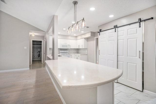 kitchen with kitchen peninsula, white appliances, a barn door, white cabinets, and hanging light fixtures