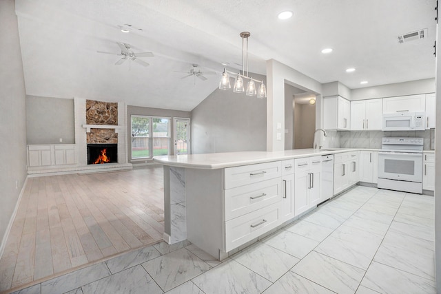 kitchen featuring a stone fireplace, kitchen peninsula, vaulted ceiling, white appliances, and white cabinets